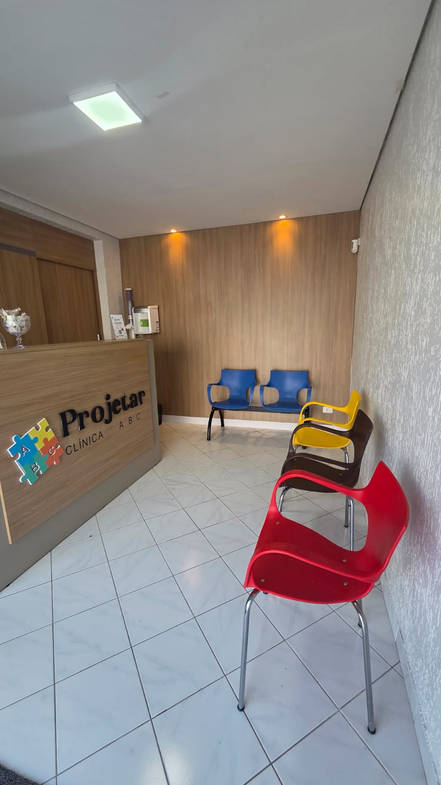Recepção real da Clínica Projetar ABC, com o logo no balcão e cadeiras coloridas